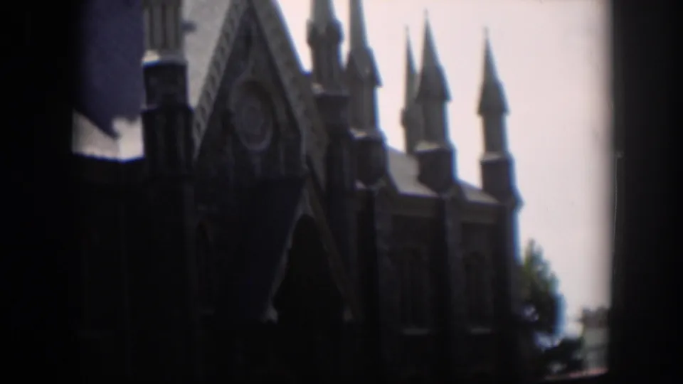 The home-movie frame shows the church's pointed roofline and spires with people partly visible near the walkway below.