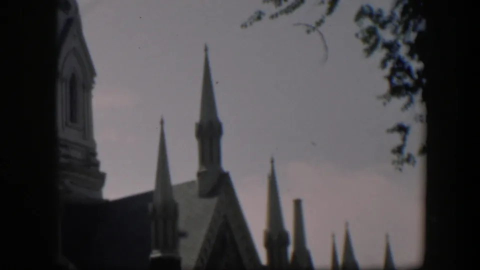 1951 Wyoming home-movie frame showing Gothic-style church spires, a steep roof, pale clouds, and nearby tree branches.