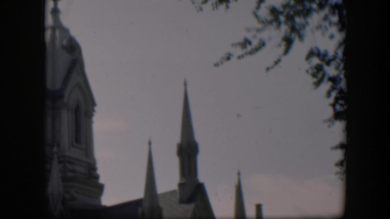 1951 Wyoming 8mm frame showing a church facade and steeples partly obscured by dark gate edges and tree shadow.