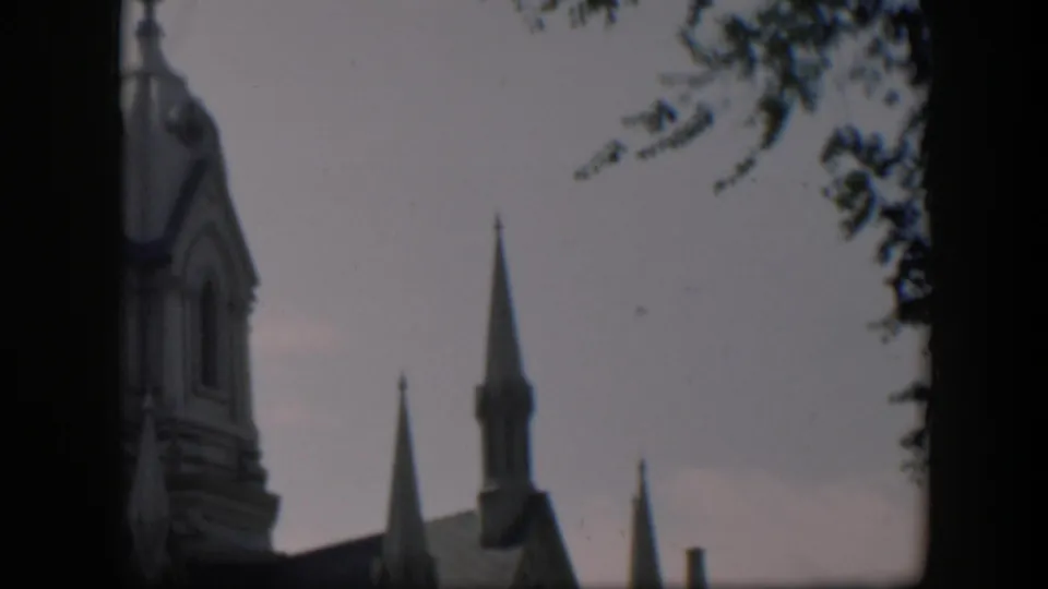 1951 Wyoming 8mm frame showing a church facade and steeples partly obscured by dark gate edges and tree shadow.