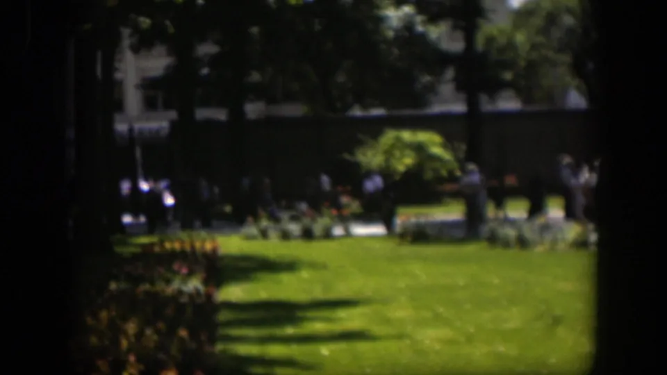 Soft 8mm view of a Wyoming park in 1951, with lawn, planting beds, shade trees and distant pedestrians by a walkway.