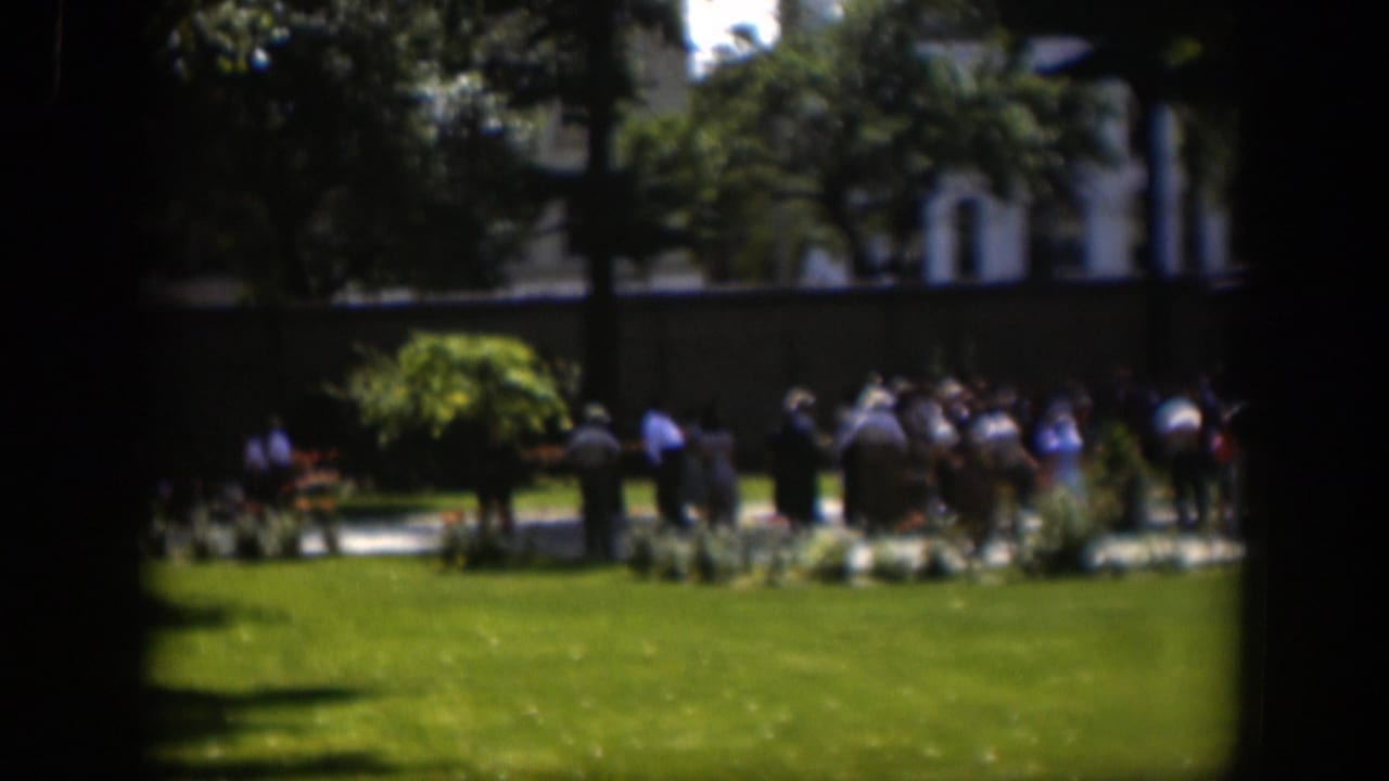 1951 Wyoming 8mm frame showing people gathered across a green park lawn, partly obscured by a dark window-like foreground.