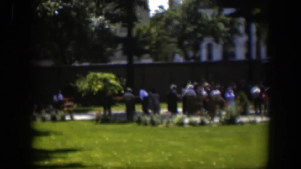 1951 Wyoming 8mm frame showing people gathered across a green park lawn, partly obscured by a dark window-like foreground.