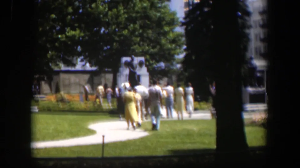 Adults in mid-century clothing walk through a landscaped Wyoming park, with trees, flowerbeds, and lawn visible in the frame.