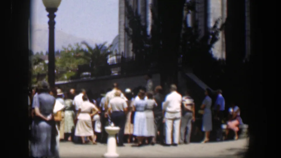 Adults in 1951 Wyoming stand outside the building, seen through dark foreground framing with a lamppost, pedestal, and trees nearby.
