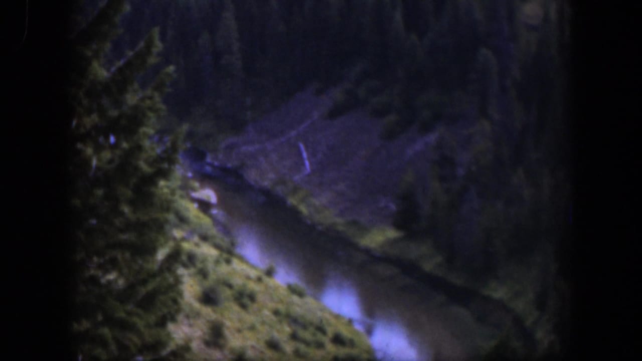1951 Wyoming home-movie frame showing a narrow stream or river curving below trees and steep banks in soft 8mm color.