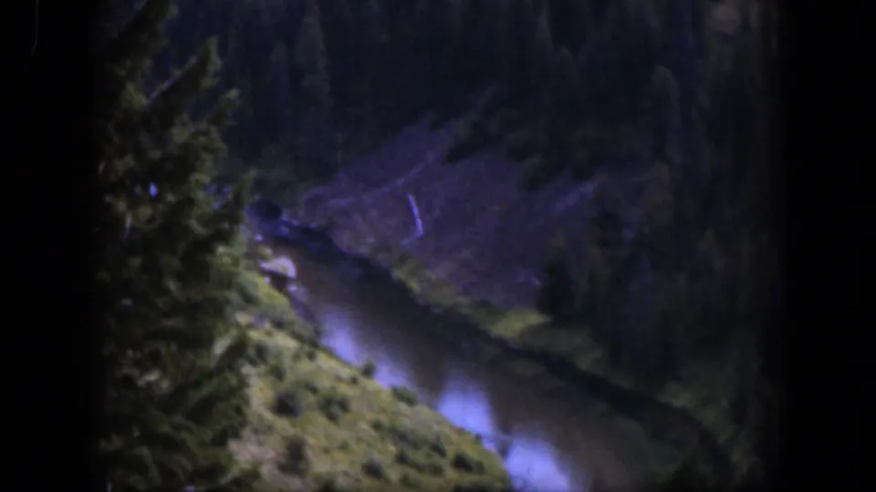 1951 Wyoming home-movie frame showing a narrow stream or river curving below trees and steep banks in soft 8mm color.