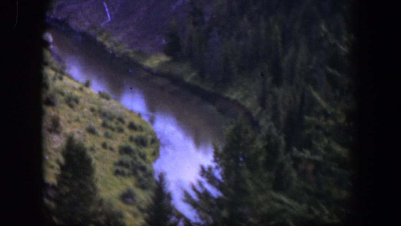 1951 Wyoming home-movie view of a pale mountain river bordered by pines and scrub-covered banks.