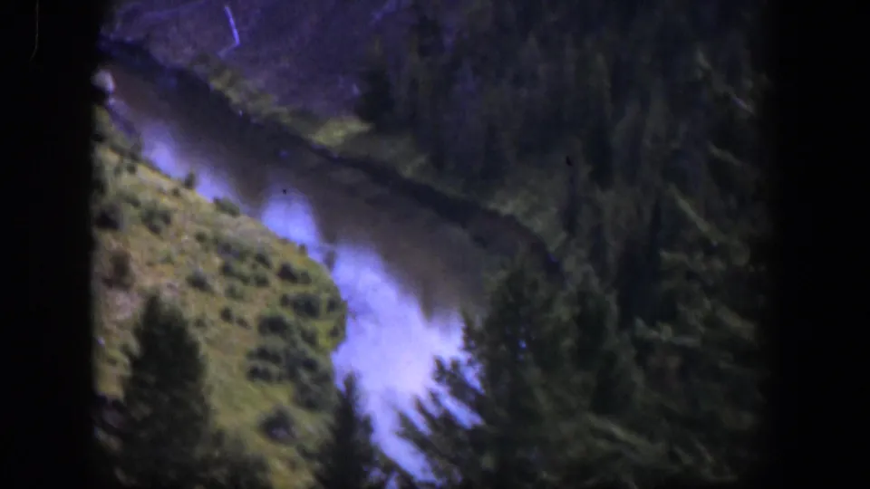 1951 Wyoming home-movie view of a pale mountain river bordered by pines and scrub-covered banks.