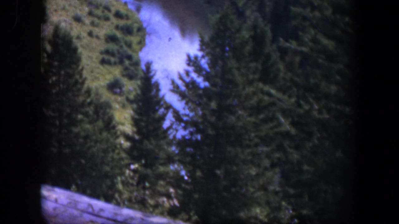 1951 Wyoming frame showing river rapids, pine forest, hillside vegetation, and a small wooden foreground edge.