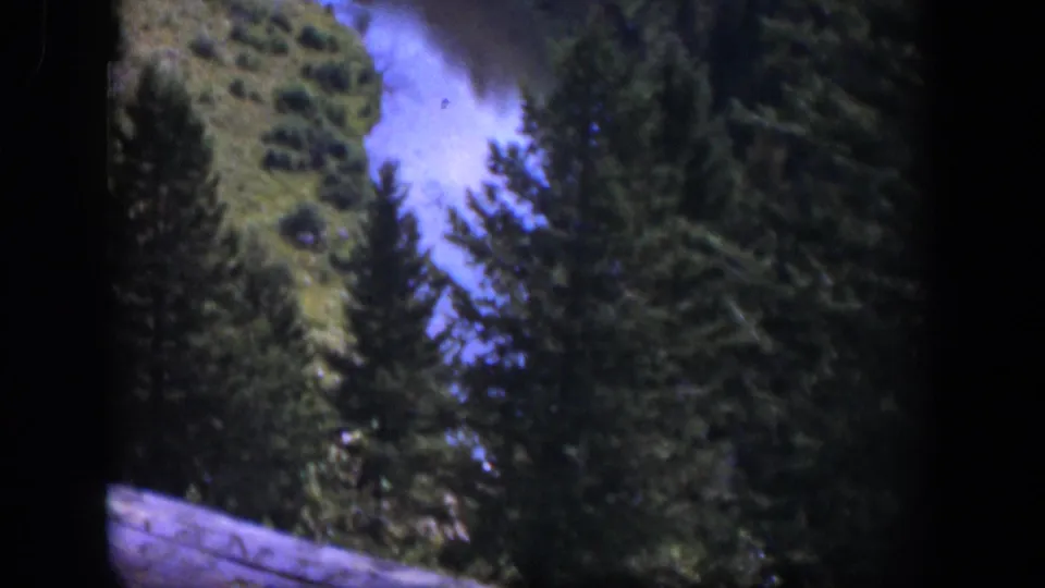 1951 Wyoming frame showing river rapids, pine forest, hillside vegetation, and a small wooden foreground edge.