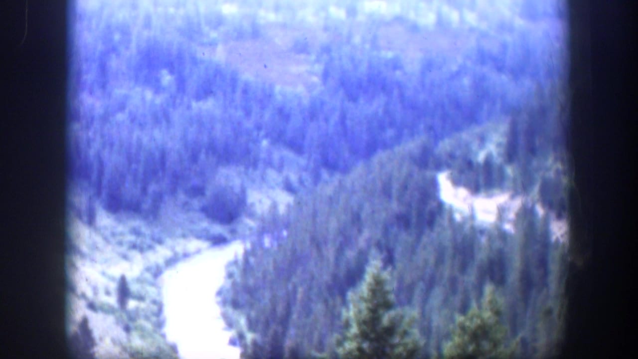 Soft 8mm view of a winding river below a forested valley with dark film borders.