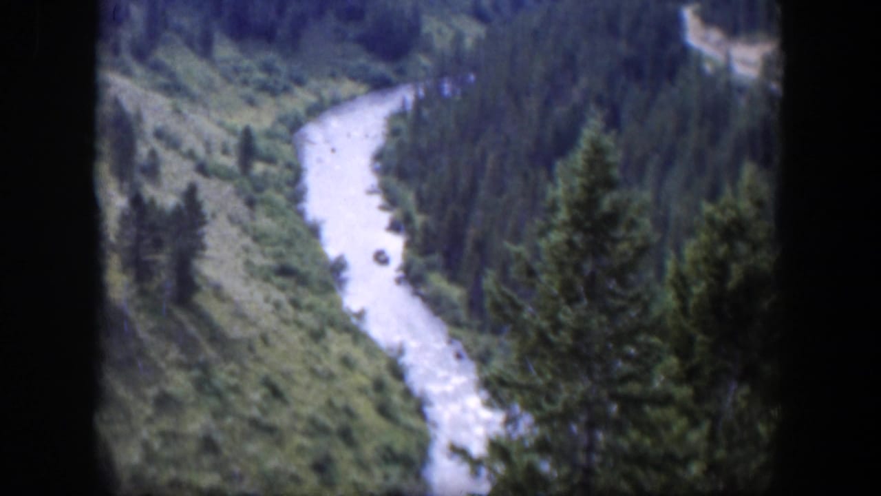 1951 Wyoming 8mm frame showing a pale river curving through a green valley bordered by evergreen forest.