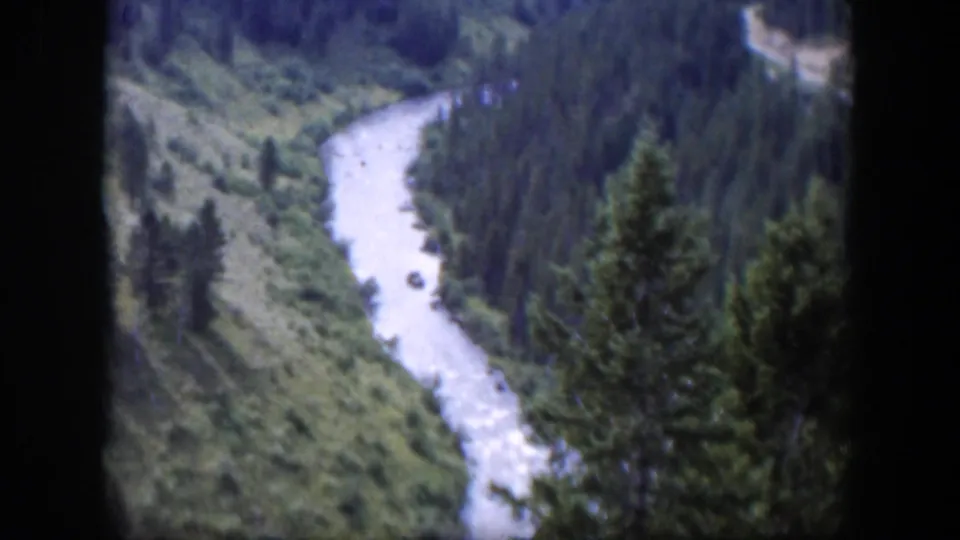 1951 Wyoming 8mm frame showing a pale river curving through a green valley bordered by evergreen forest.