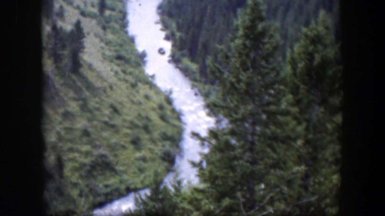 1951 Wyoming 8mm frame showing a pale river running below evergreen trees and green valley terrain.