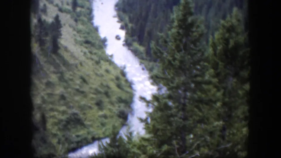 1951 Wyoming 8mm frame showing a pale river running below evergreen trees and green valley terrain.