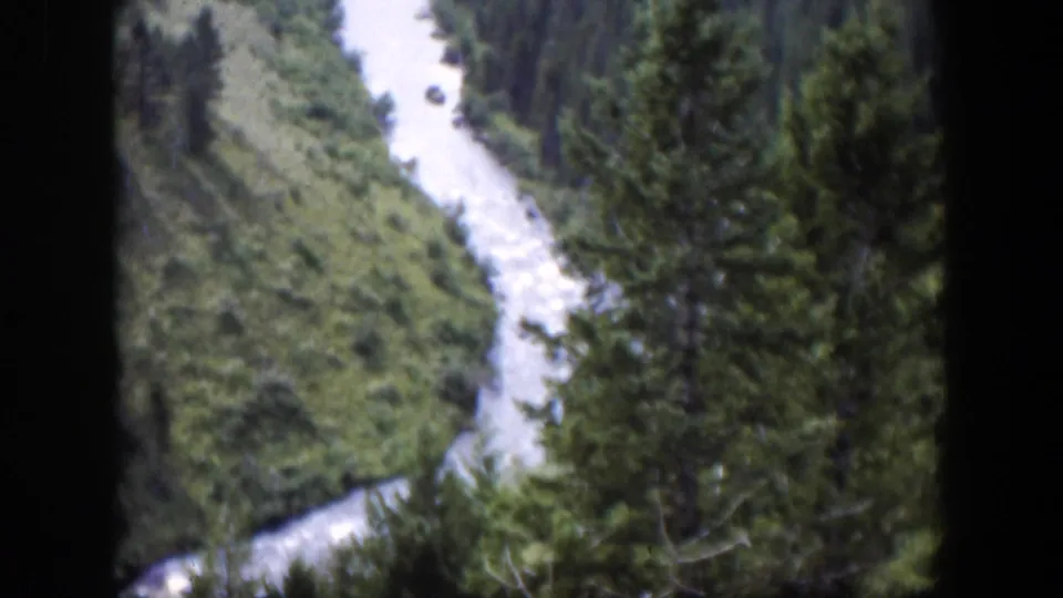 1951 Wyoming 8mm frame of a winding river beside evergreen trees, viewed from above in a mountain valley.