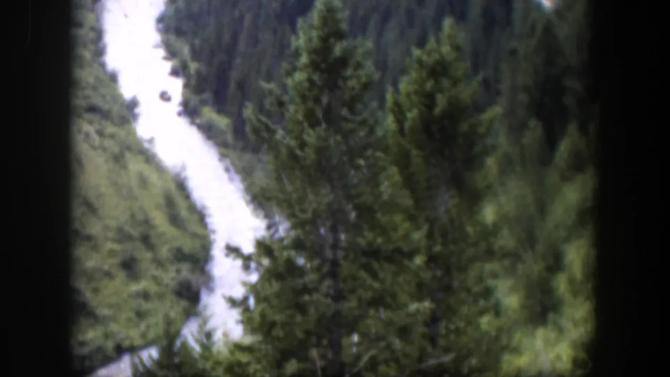 1951 Wyoming 8mm frame showing a narrow bright river channel descending through dense forested slopes.