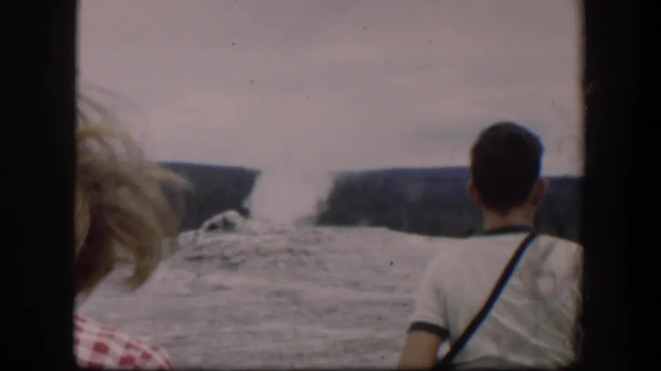 A man in a light shirt and a blonde woman in a checkered top face a Wyoming waterfall scene in 1951 home-movie footage.