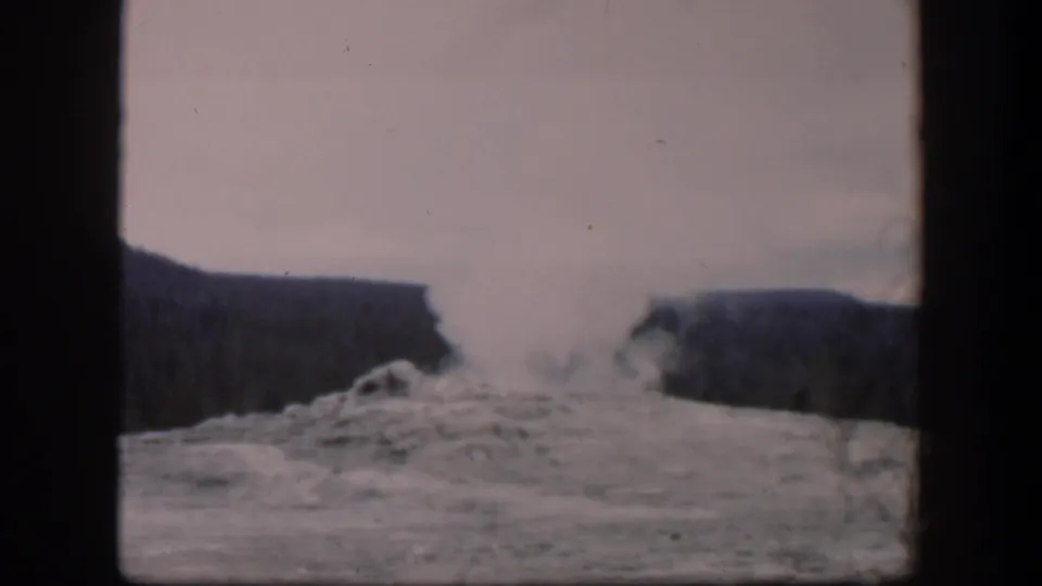 1951 Wyoming 8mm frame holding on the geyser-like plume as steam drifts upward from the rocky ground below a wooded ridge.