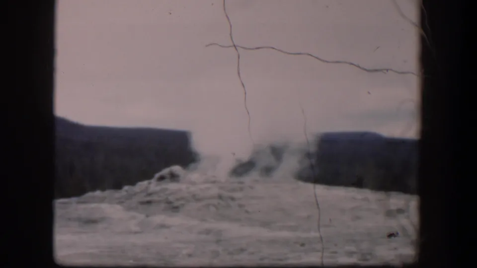 1951 Wyoming home-movie frame showing drifting steam over a rocky geyser area, with dark ridges, soft focus, and visible film scratches.