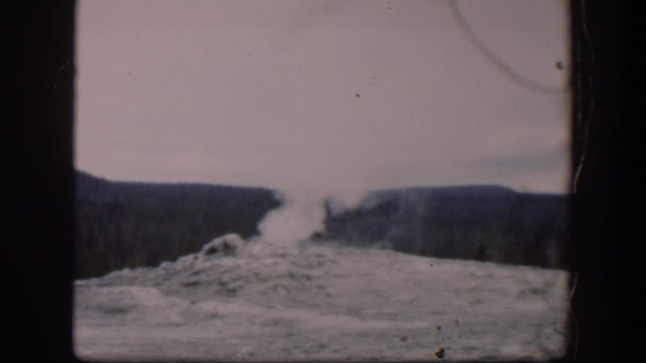 Steam plume drifts upward over rocky ground and distant dark hills.