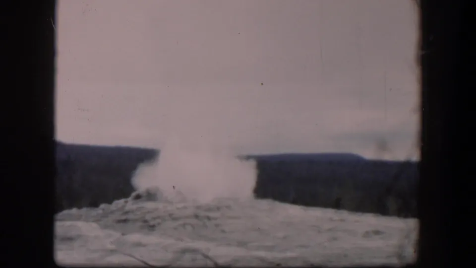 1951 Wyoming 8mm frame showing a bright steam column rising from a geyser area with dark ridges on both sides.