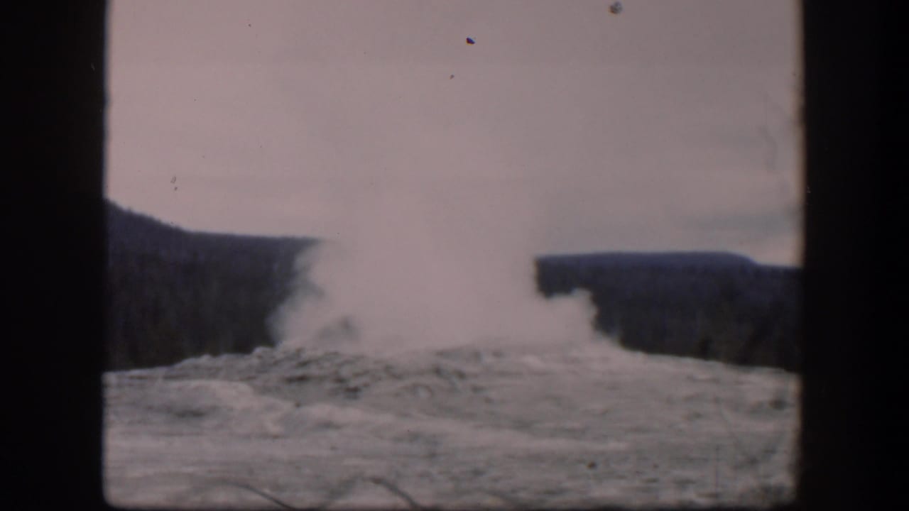Thick white steam billows upward from a geyser between dark ridges.