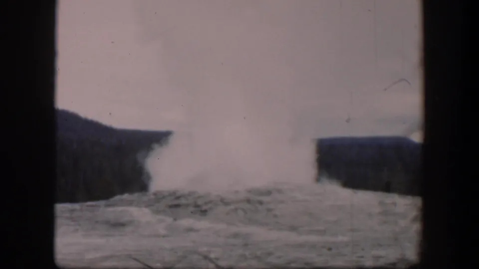1951 Wyoming 8mm frame showing the geyser eruption continuing, with white steam over pale ground and dark hills.