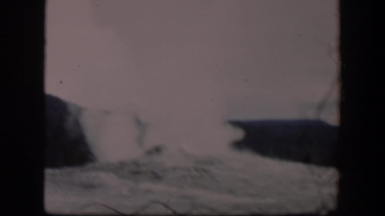 Steam plume expands near dark hillside shapes under a pale sky.