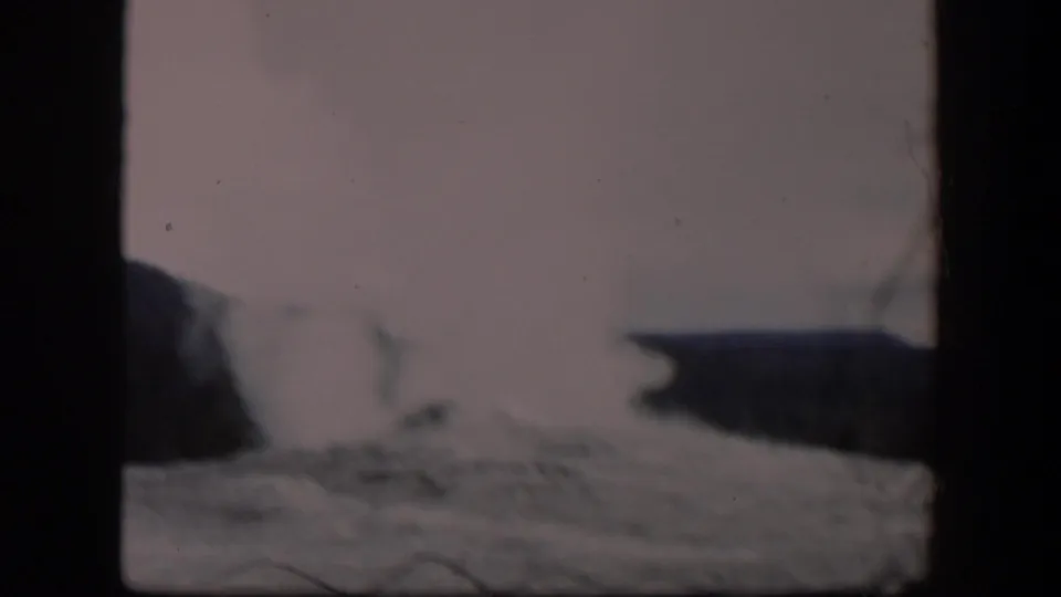 1951 Wyoming 8mm frame with a growing geyser steam cloud, low terrain, dark distant hills, and visible film-frame borders.