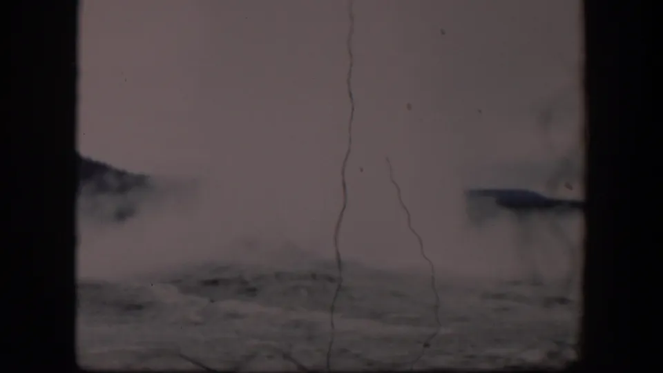 1951 Wyoming 8mm frame showing drifting geyser steam over low rocky terrain, with muted color, scratches, and strong gate-edge shadows.
