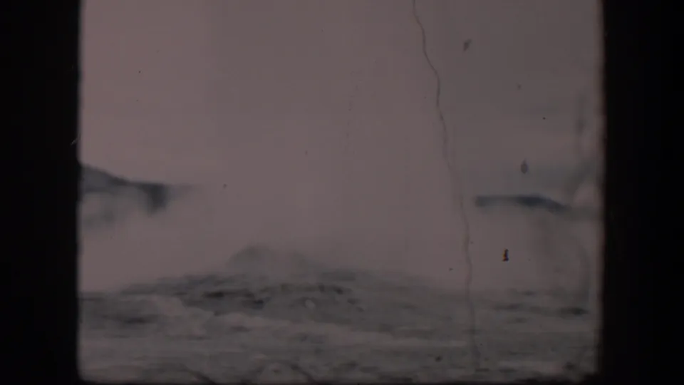 1951 Wyoming home-movie frame showing geyser steam drifting over gray rocks beneath an overcast sky.