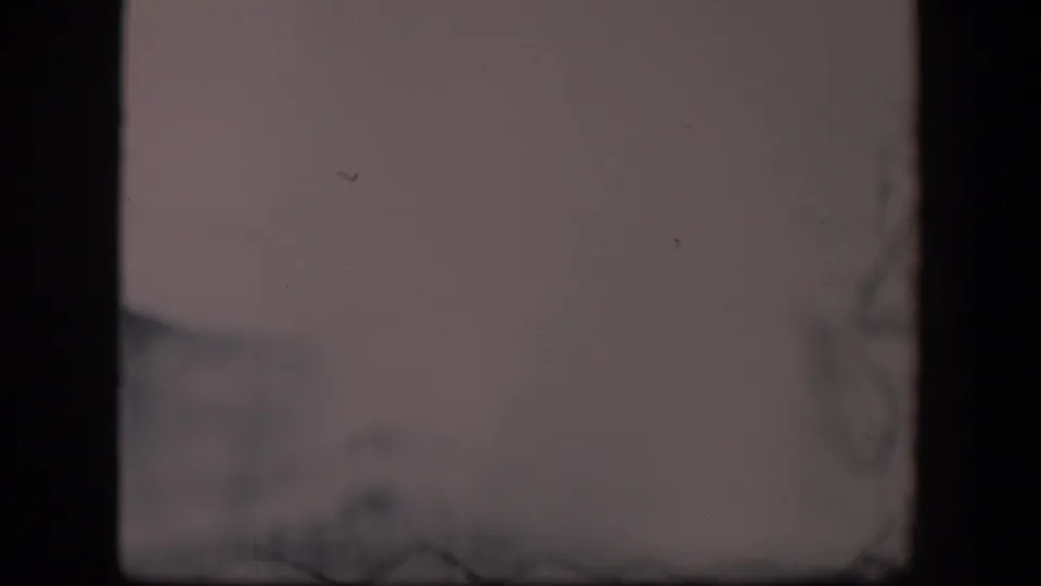 Soft 8mm frame from Wyoming showing faint geyser vapor and blurred gray ground under cloudy light.