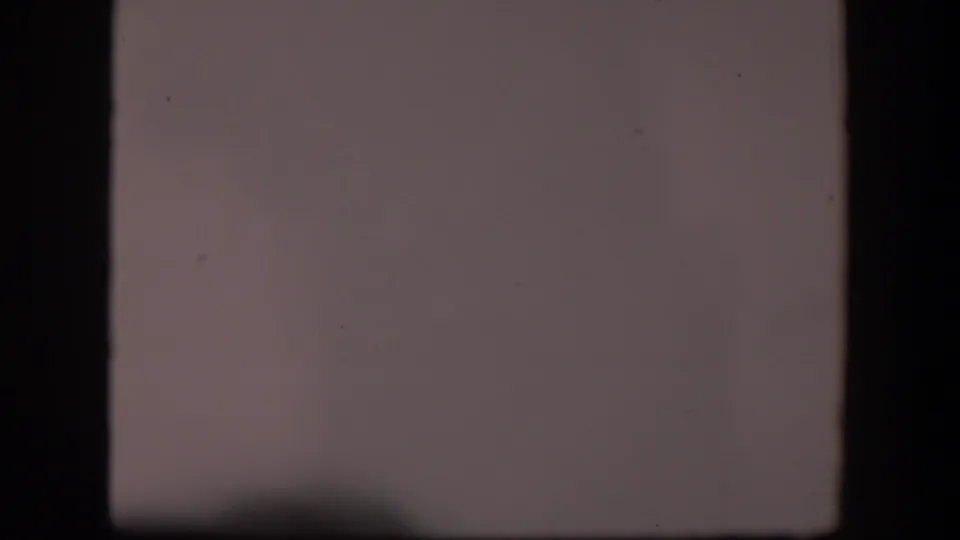 1951 Wyoming 8mm frame showing pale sky or overexposed desert view with dark film borders, dust, and faint terrain along the lower edge.