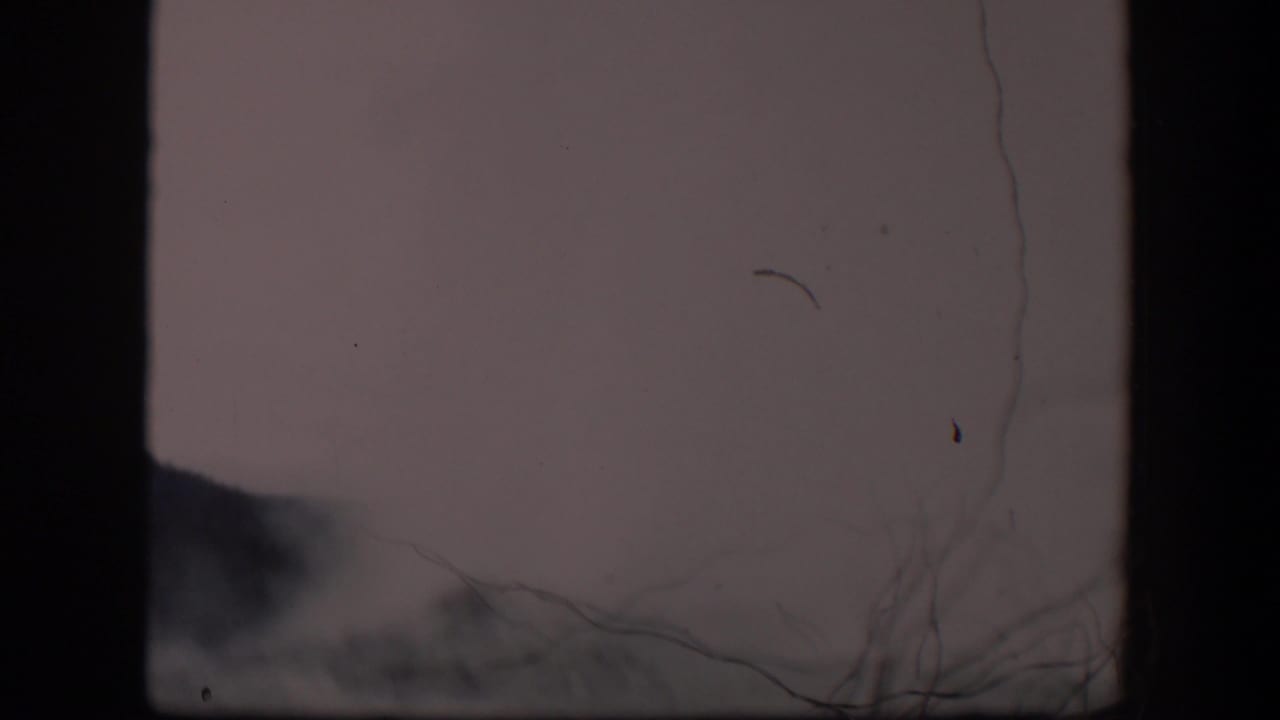 Hazy distant dark hill or mountain behind heavy scratches and film debris.