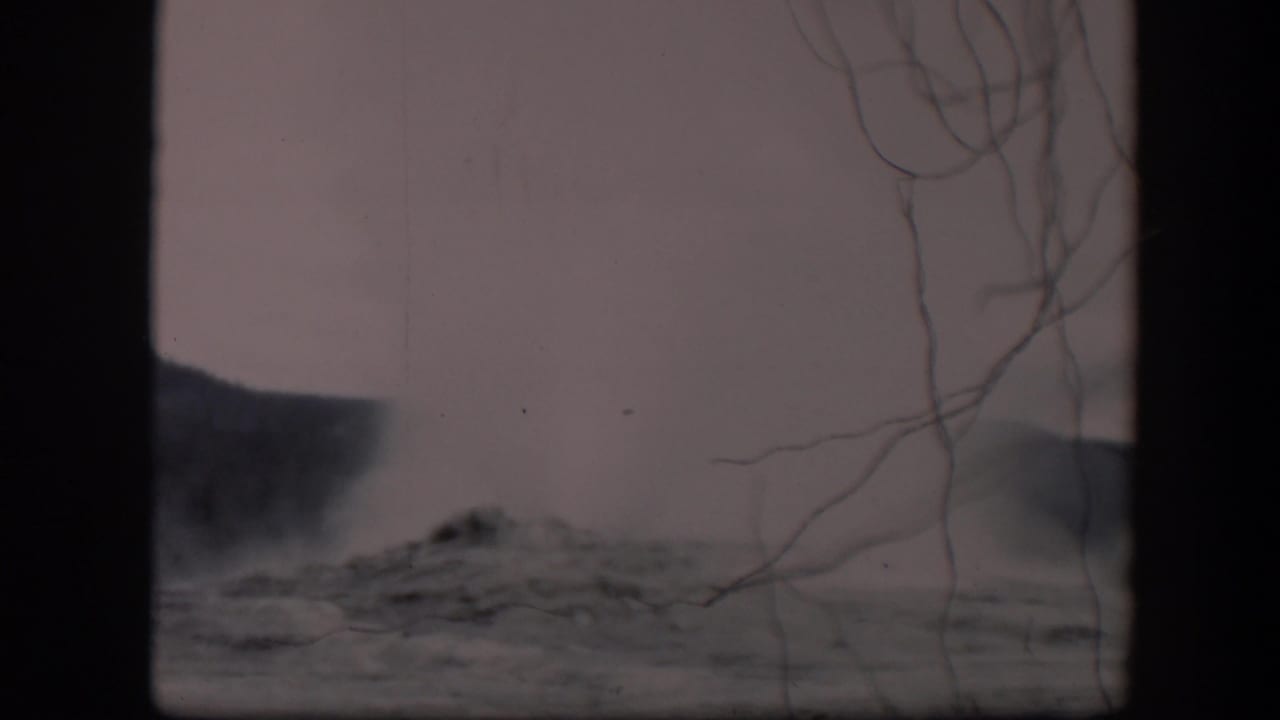 Distant dark ridge or plume area, pale sky, branches, and dark frame bars.