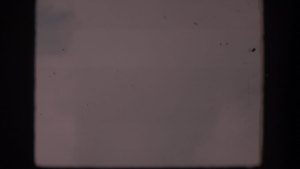 1951 Wyoming 8mm frame with a muted pale view, faint haze, visible dust specks, and dark gate edges around an indistinct open landscape.