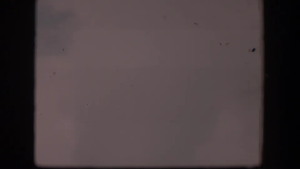 1951 Wyoming 8mm frame with a muted pale view, faint haze, visible dust specks, and dark gate edges around an indistinct open landscape.