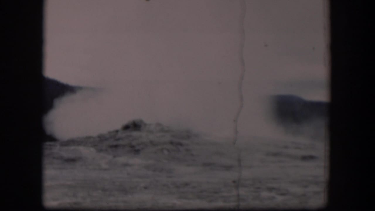 1951 Wyoming 8mm frame showing a pale dust or steam plume lifting from dark rocky terrain, with haze, scratches, and gate borders visible.