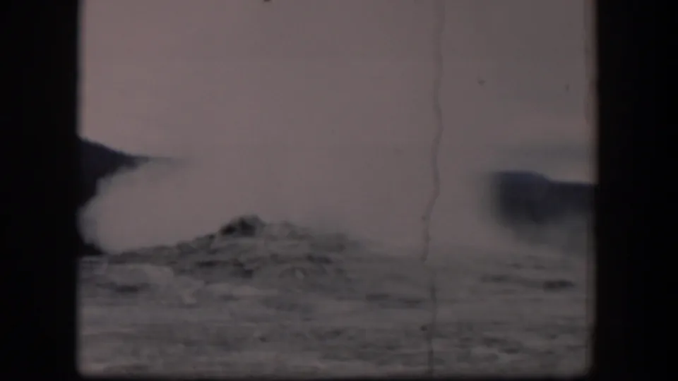 1951 Wyoming 8mm frame showing a pale dust or steam plume lifting from dark rocky terrain, with haze, scratches, and gate borders visible.