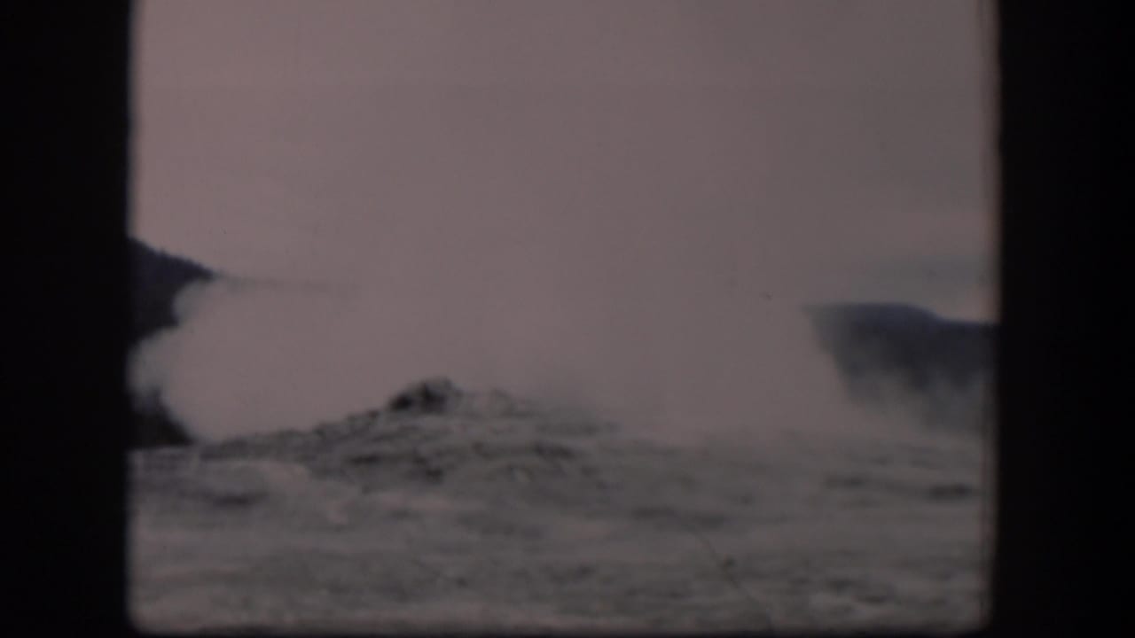 Old Faithful geyser plume rising above rocky ground in a hazy 8mm frame.