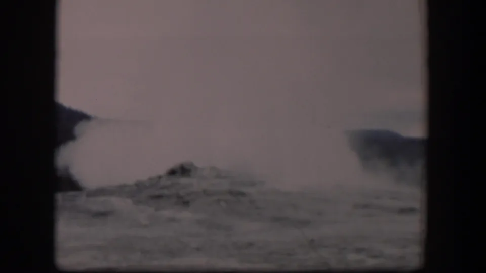 1951 8mm Yellowstone footage showing Old Faithful steam and water rising behind dark rocky terrain.