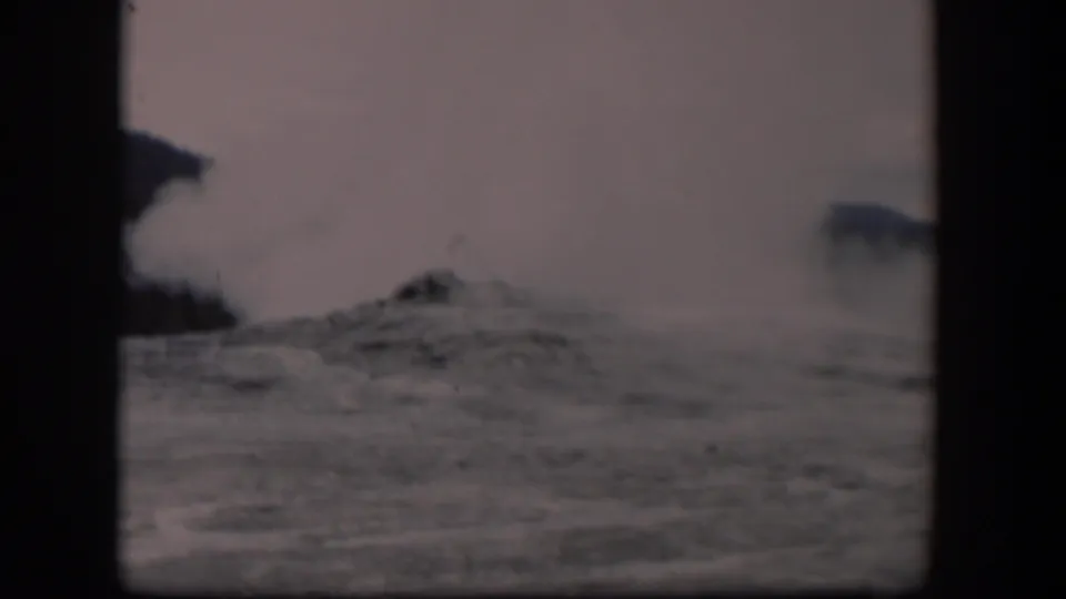 Old Faithful appears mid-eruption in Yellowstone, with steam drifting across a pale sky and rocky ground below.