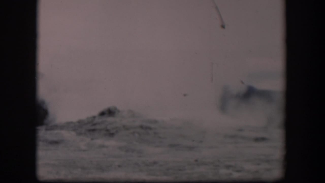 A visitor-shot 1951 8mm frame shows Old Faithful steam dispersing over Yellowstone’s rough geyser basin surface.