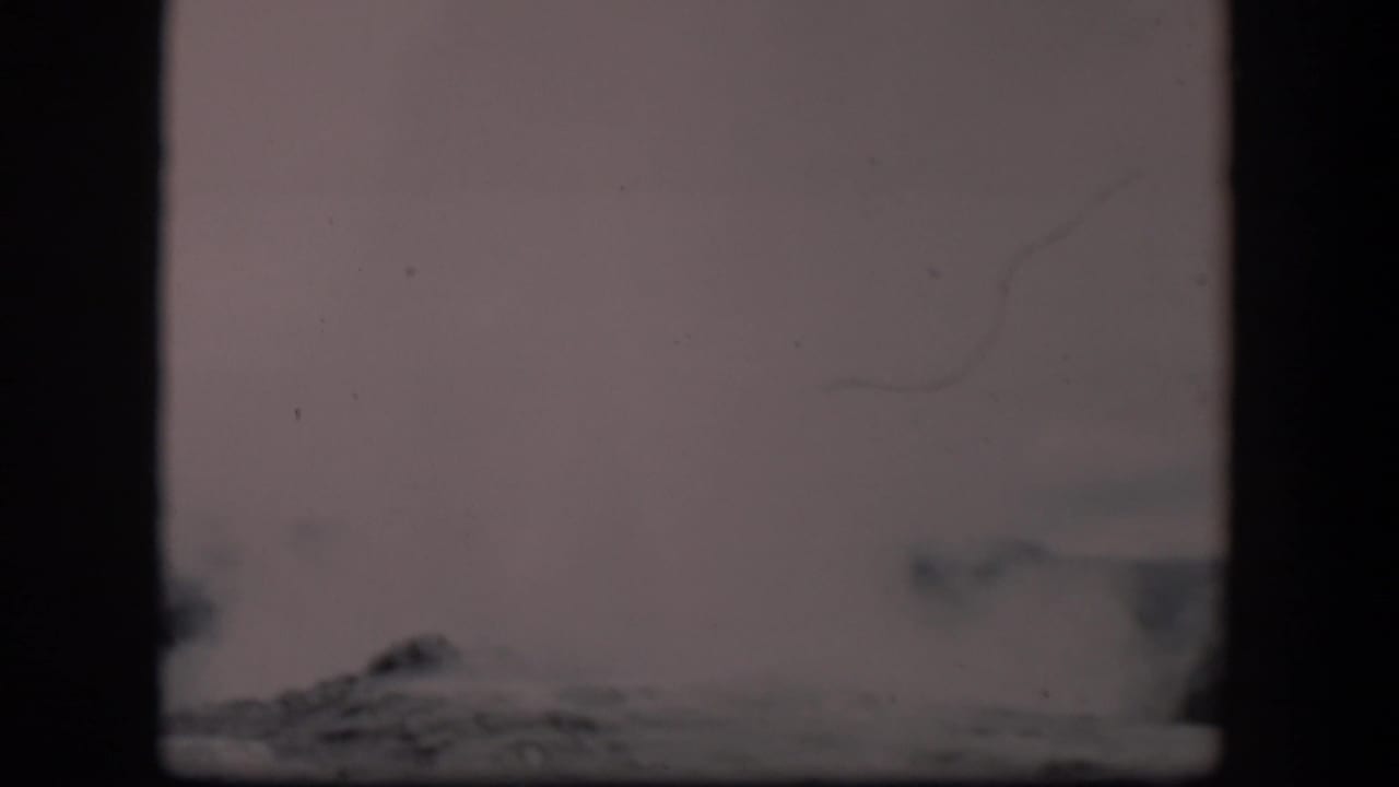 Late in the clip, the Old Faithful plume is partly low in frame, with pale sky, film scratches, and dark frame borders visible.