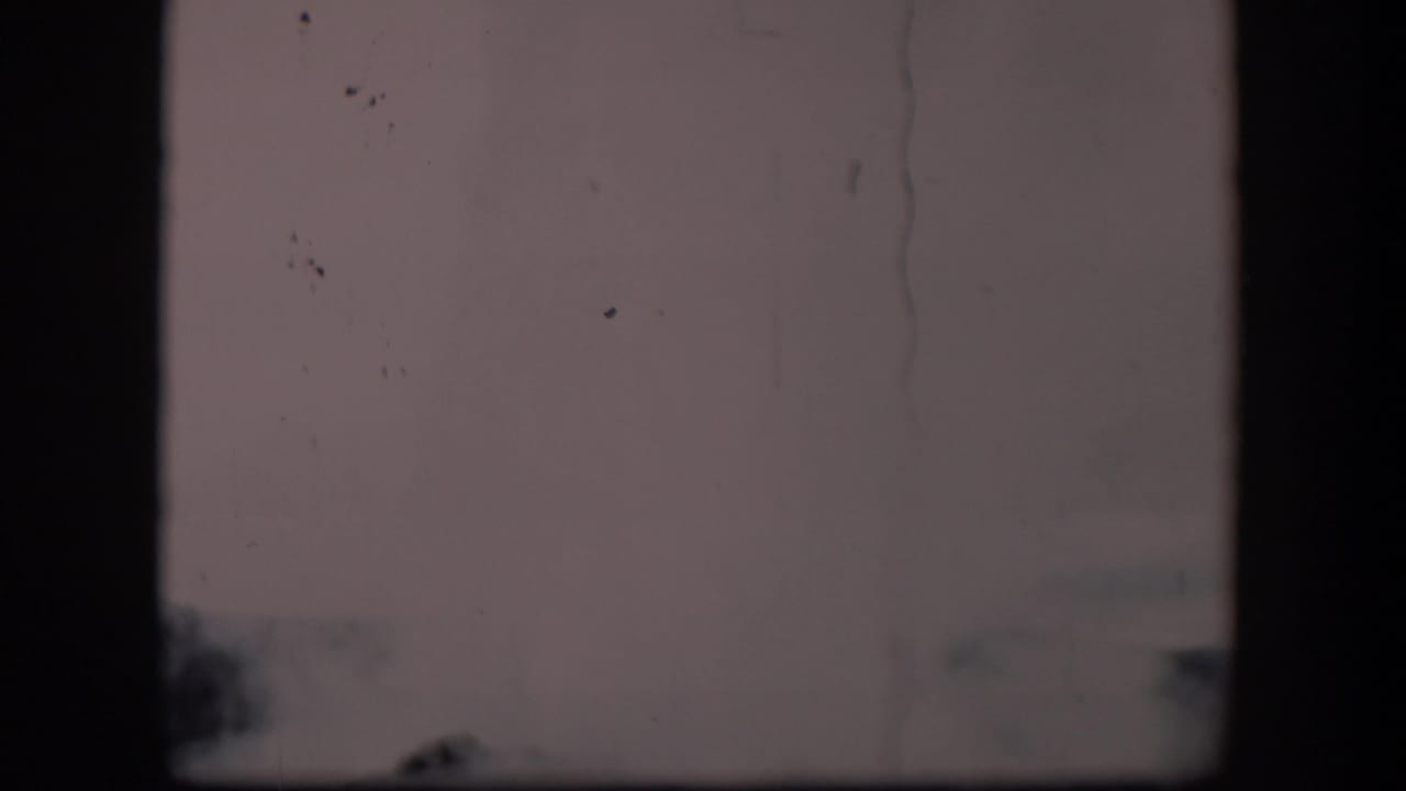 Obscured 1951 Wyoming 8mm frame with dark film edges, pale sky, faint trees, and a partial distant roofline.