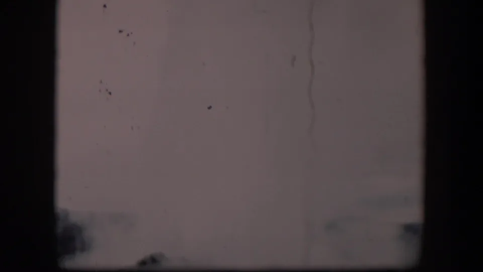 Obscured 1951 Wyoming 8mm frame with dark film edges, pale sky, faint trees, and a partial distant roofline.