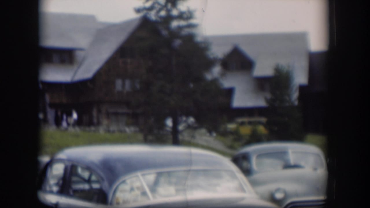 1951 Wyoming 8mm frame showing parked vintage cars in the foreground, a yellow vehicle, trees, and a brown sloped-roof building.