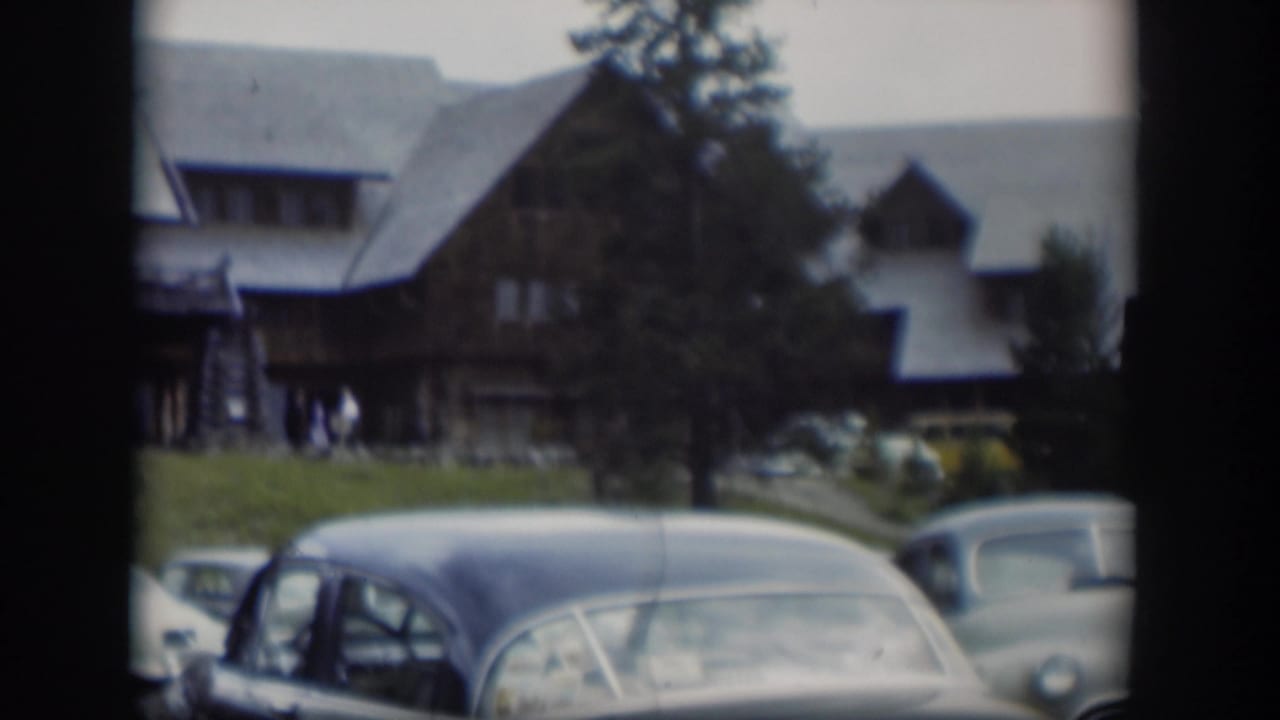 Vintage cars parked on a lawn in front of a large log lodge.